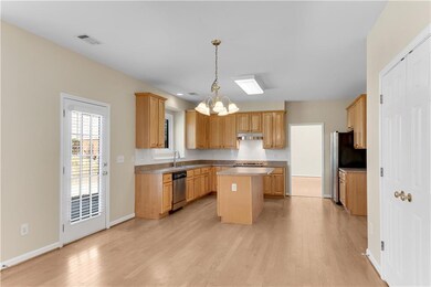 Kitchen with a kitchen island, stainless steel appliances, a chandelier, light wood-style floors, and baseboards