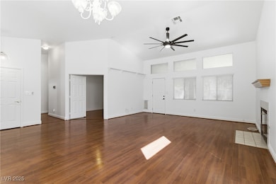 Unfurnished living room featuring a fireplace with flush hearth, dark wood-type flooring, a chandelier, high vaulted ceiling, and ceiling fan