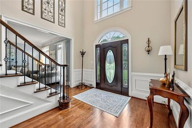 Grand two-story foyer featuring beautifully finished hardwood floors, decorative wainscoting, and a stunning leaded glass door.