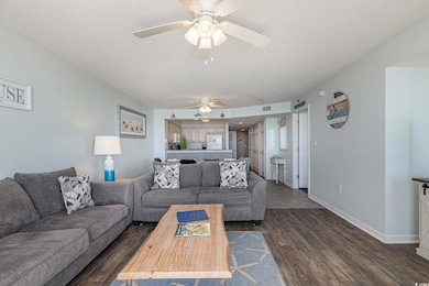 Living area with a textured ceiling, dark wood-style floors, and ceiling fan
