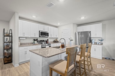 Kitchen with light wood finished floors, appliances with stainless steel finishes, a breakfast bar area, white cabinets, and an island with sink