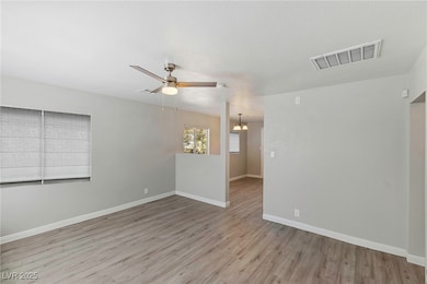 Spare room featuring light wood-style flooring, a chandelier, and a ceiling fan