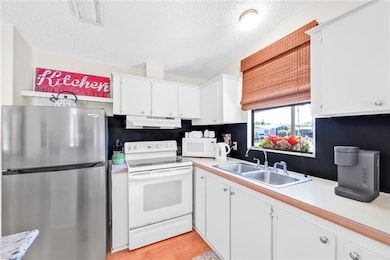 Kitchen with under cabinet range hood, white appliances, light countertops, and a sink