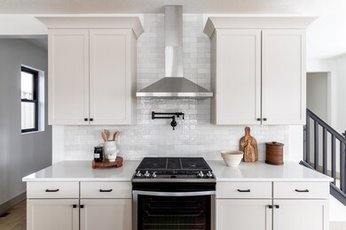 Kitchen with stainless steel gas stove, wall chimney range hood, tasteful backsplash, and white cabinetry