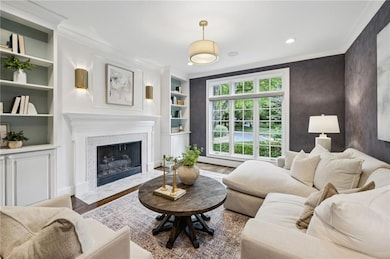 Living room featuring built in features, a premium fireplace, ornamental molding, wood finished floors, and a baseboard radiator