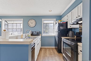 Kitchen with black appliances, white cabinets, a textured ceiling, light countertops, and light wood-type flooring