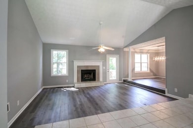 Unfurnished living room with lofted ceiling, healthy amount of natural light, a tile fireplace, wood finished floors, and a ceiling fan