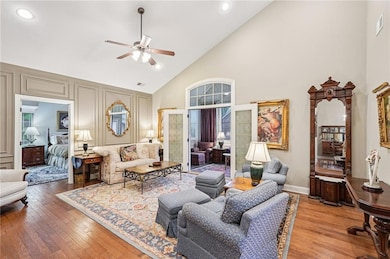 Living area featuring high vaulted ceiling, hardwood / wood-style floors, ceiling fan, recessed lighting, and a decorative wall