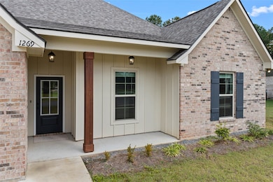 View of exterior entry featuring a shingled roof, covered porch, brick siding, and board and batten siding