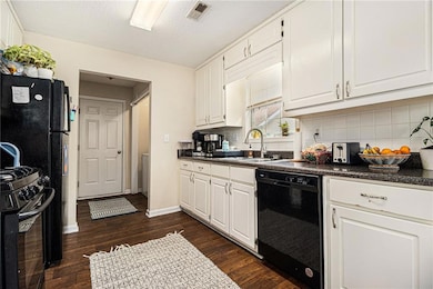Kitchen with dark countertops, black appliances, white cabinetry, dark wood-style floors, and a textured ceiling