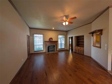 Unfurnished living room featuring dark wood finished floors, ornamental molding, a fireplace with flush hearth, and ceiling fan