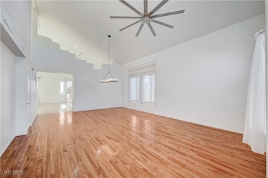 Unfurnished living room with high vaulted ceiling, light wood-style flooring, and a chandelier