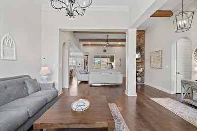Living room with a chandelier, arched walkways, dark wood-type flooring, decorative columns, and crown molding