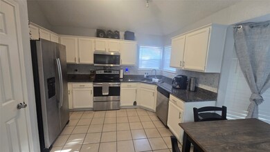 Kitchen with appliances with stainless steel finishes, white cabinetry, light tile patterned floors, and dark stone counters