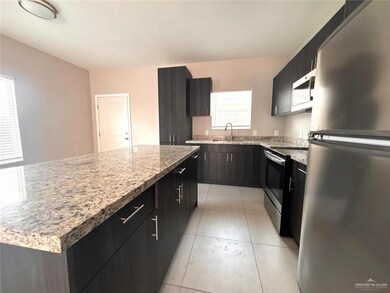 Kitchen with appliances with stainless steel finishes, a kitchen island, light tile patterned flooring, and light stone counters