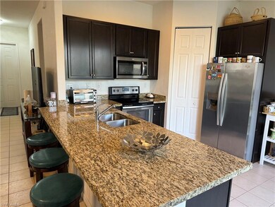 Kitchen with light tile patterned floors, a peninsula, a kitchen breakfast bar, stainless steel appliances, and dark stone counters