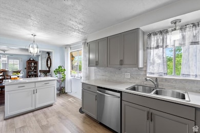 Kitchen with dishwasher, gray cabinets, a sink, a textured ceiling, and healthy amount of natural light