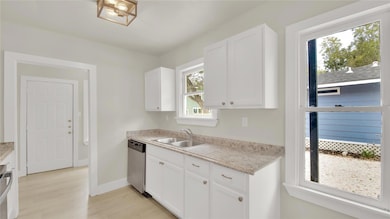 Kitchen featuring white cabinetry, stainless steel dishwasher, light wood-type flooring, and light stone countertops