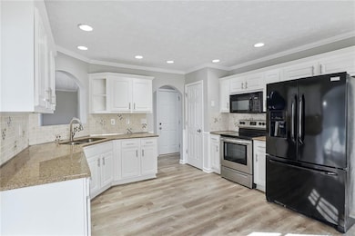 Kitchen featuring black appliances, arched walkways, white cabinets, light stone countertops, and recessed lighting
