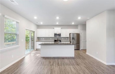 Kitchen featuring stainless steel appliances, white cabinetry, light wood-style floors, a kitchen island with sink, and recessed lighting