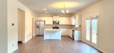 Kitchen featuring a kitchen island, white cabinetry, appliances with stainless steel finishes, decorative light fixtures, and an inviting chandelier