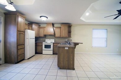 Kitchen with white appliances, a peninsula, ceiling fan, a kitchen breakfast bar, and light tile patterned floors
