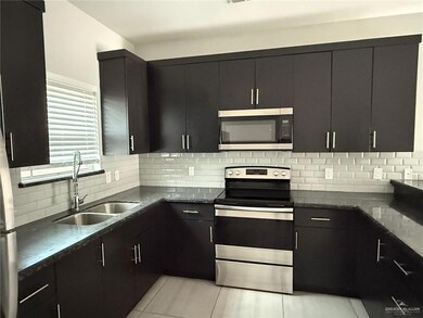 Kitchen featuring stainless steel appliances, tasteful backsplash, a sink, dark cabinets, and dark stone counters