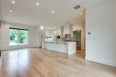 Kitchen featuring white cabinetry, open floor plan, a large island with sink, a kitchen breakfast bar, and built in fridge