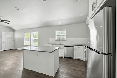 Kitchen featuring stainless steel appliances, white cabinets, backsplash, dark stone counters, and a kitchen island