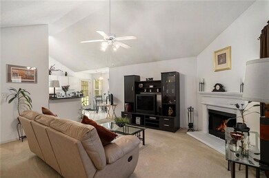 Living room featuring vaulted ceiling, light colored carpet, ceiling fan, a lit fireplace, and baseboards