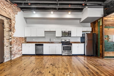 Kitchen featuring stainless steel appliances, a sink, white cabinetry, light wood-type flooring, and brick wall