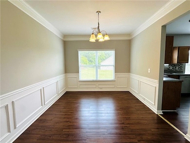 Unfurnished dining area featuring a chandelier, dark wood-style flooring, a wainscoted wall, a decorative wall, and crown molding