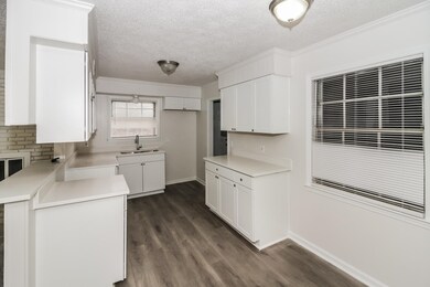 Kitchen with a textured ceiling, dark wood finished floors, white cabinetry, light countertops, and ornamental molding