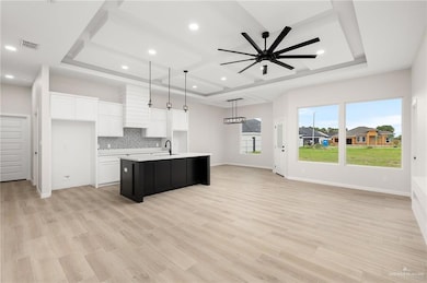 Kitchen with hanging light fixtures, a kitchen island with sink, ceiling fan, white cabinets, and backsplash