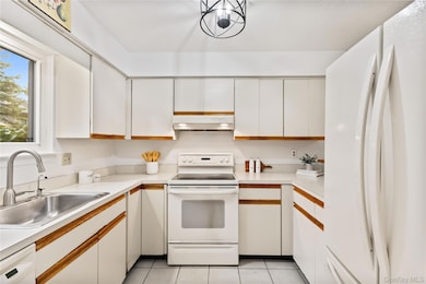 Kitchen featuring white cabinets, white appliances, light countertops, and brown cabinets