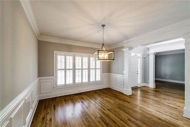 Unfurnished dining area with a chandelier, ornate columns, wood finished floors, wainscoting, and ornamental molding