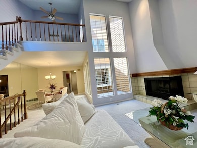 Living area featuring carpet floors, a high ceiling, a tiled fireplace, ceiling fan, and a chandelier