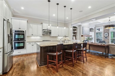 Kitchen featuring stainless steel appliances, open floor plan, white cabinetry, dark wood-type flooring, and crown molding