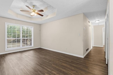 Unfurnished room with a tray ceiling, dark wood finished floors, ceiling fan, and a textured ceiling