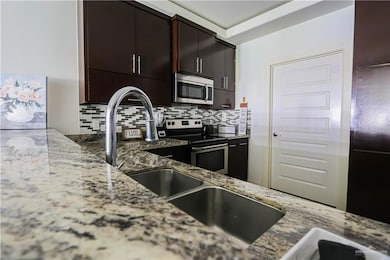 Kitchen featuring stainless steel appliances, light stone counters, and decorative backsplash