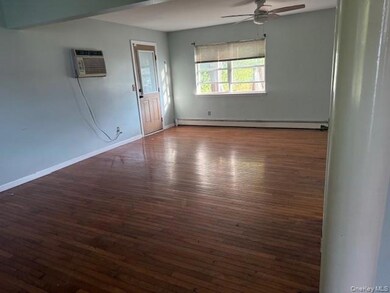 Empty room with dark wood finished floors, ceiling fan, baseboard heating, and an AC wall unit