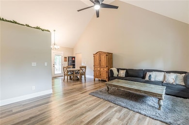 Living area featuring high vaulted ceiling, a ceiling fan, light wood-style floors, and a chandelier