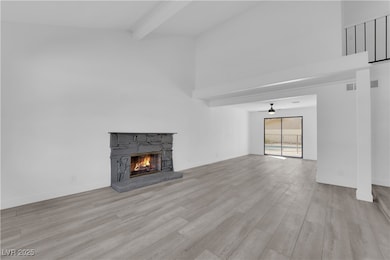 Unfurnished living room with beamed ceiling, a high ceiling, a stone fireplace, and light wood-type flooring