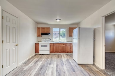 Kitchen with white appliances, light countertops, brown cabinetry, and light wood-type flooring
