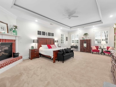 Bedroom featuring a raised ceiling, crown molding, carpet floors, recessed lighting, and a fireplace