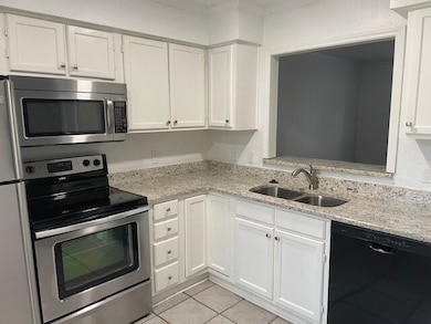 Kitchen featuring stainless steel appliances, white cabinets, light stone countertops, and light tile patterned floors