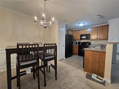 Kitchen with a chandelier, crown molding, black appliances, light colored carpet, and light countertops