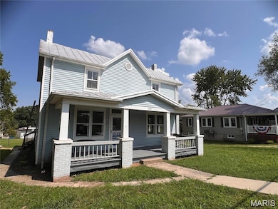 View of front of home featuring a porch, a standing seam roof, a front lawn, a metal roof, and a chimney