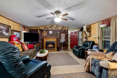 Living area with wood walls, a brick fireplace, lofted ceiling, a textured ceiling, and ceiling fan