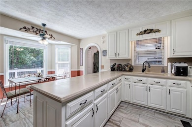 Kitchen featuring a textured ceiling, white cabinets, arched walkways, a peninsula, and ceiling fan